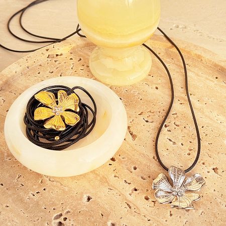 Both gold and silver hibiscus pendants displayed on a stone surface.