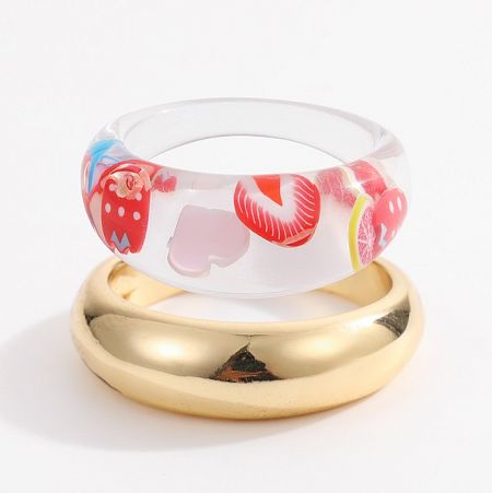 A clear plastic bracelet with colorful fruit designs paired with a stackable gold ring from the collection.
