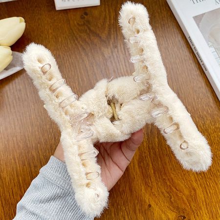 A hand holding a large, cozy khaki-colored fuzzy hair clip to show its size and texture.