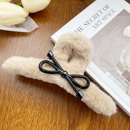 A stylish beige fuzzy hair clip accented with a contrasting black bow.