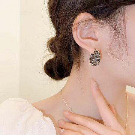 Model showcasing geometric gold earrings with clear stones.