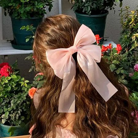 A young girl wearing a large light pink satin bow hair clip.
