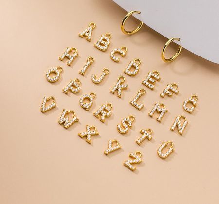 Close-up of gold alphabet letter charms for the initial hoop earrings, embellished with white stones.