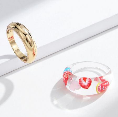 Fruit Acrylic With Metal Stackable Band Ring Set - A product shot of the Fruit Acrylic and Metal Stackable Band Ring Set, featuring a clear acrylic ring with fruit designs alongside a complementary gold metal band.