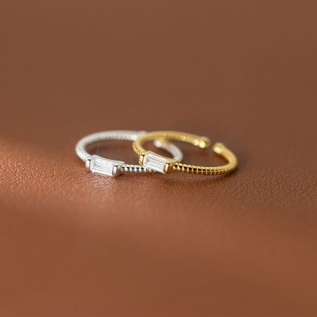 Gold and silver twisted rope rings with rectangular gemstones displayed on a textured leather surface.