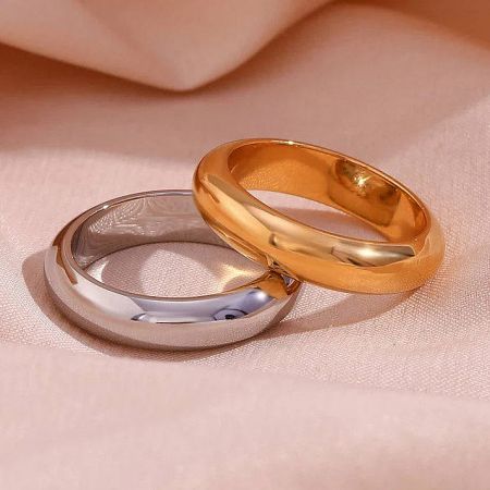 The gold and silver stainless steel band rings displayed on a soft pink background.