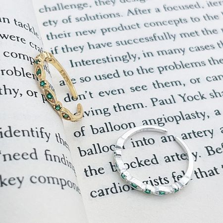 The set of five green zircon stacking rings in silver and gold, elegantly displayed on a book.