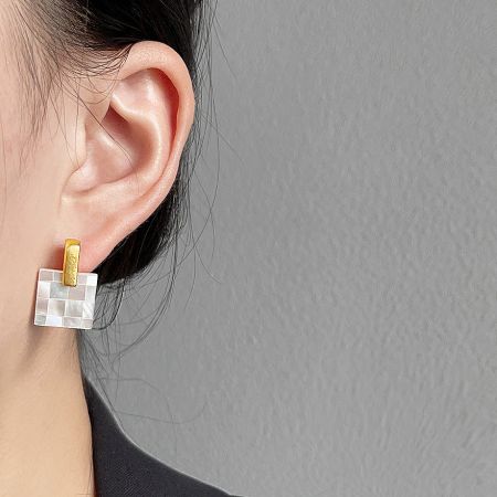 Close-up of a square mosaic stud earring with a gold and white checkered mother of pearl shell pattern.