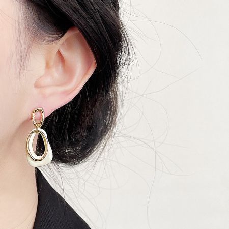 Close-up of the geometric white enamel and gold drop earring being worn to show scale and style.