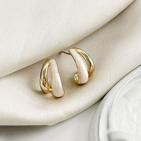 Close-up product photo of the curved gold and white earrings on a cream fabric.