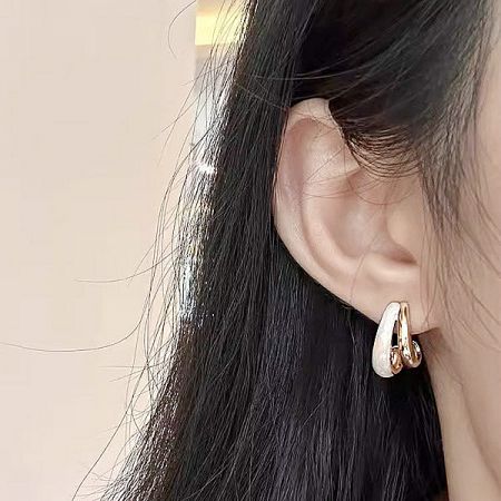 Detailed close-up of a woman wearing the gold and white enamel earring.