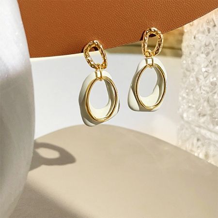 A detailed studio shot of the pair of geometric overlapping white and gold earrings.