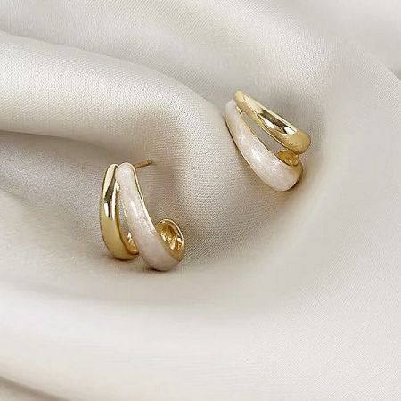 Elegant presentation of the gold and white earrings on a luxurious fabric.