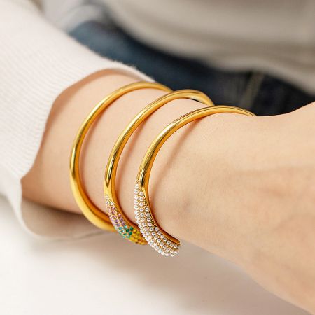 A collection of four gold open cuff bangles with pearl and stone details.