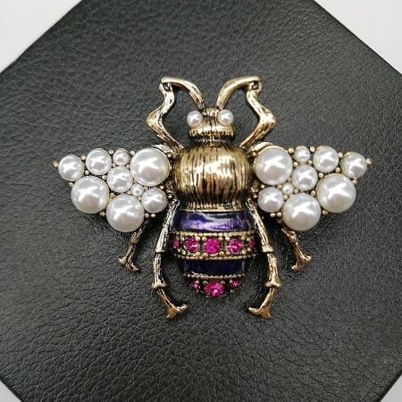 Vintage Bronze Bee Brooch with Pearl & Yellow Enamel – Galaxy Memory Collection (5 pcs) - A detailed close-up of the Vintage Bronze Bee Brooch, highlighting its antique gold finish, faux pearl wings, and purple enamel body with magenta rhinestone accents.