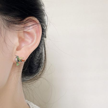 Close-up of a woman wearing a 14k gold-plated bee stud earring with green and clear zircon details.
