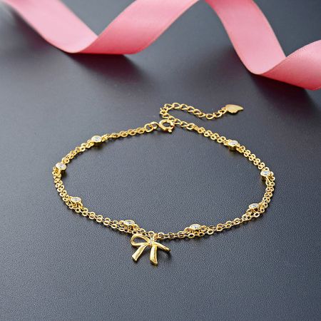 Detailed view of the gold-plated bow charm bracelet, highlighting the clear gemstones and intricate chain.