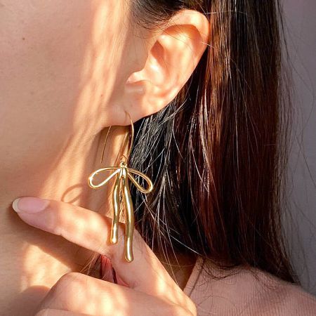 A detailed close-up of the gold bow earring, highlighting its polished finish.
