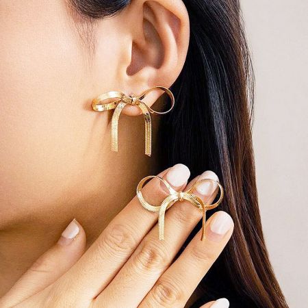 Close-up of a model wearing the gold bow earring, showing its texture and shine.