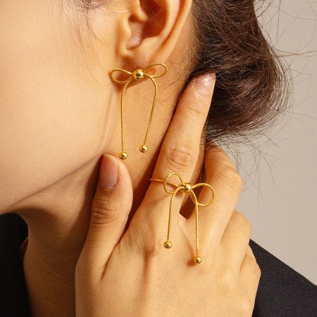 The gold knot bow earrings displayed alongside a matching ring.