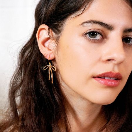 A close-up portrait of a model wearing the elegant gold knot bow drop earrings.