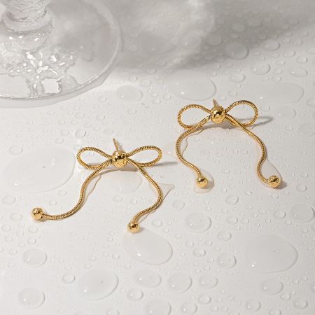 Professional product shot of the gold bow earrings on a reflective surface.