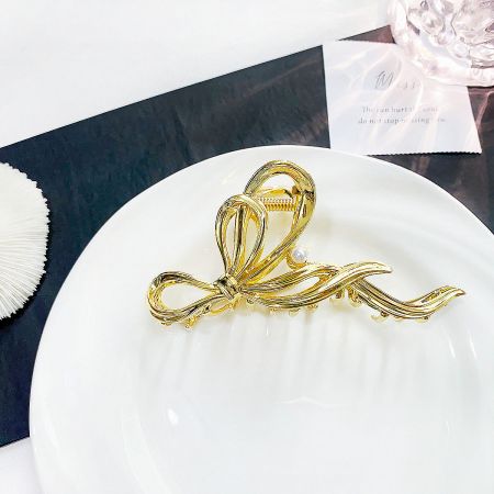 Close-up of the gold metal ribbon hair clip with a central pearl accent on a white plate.