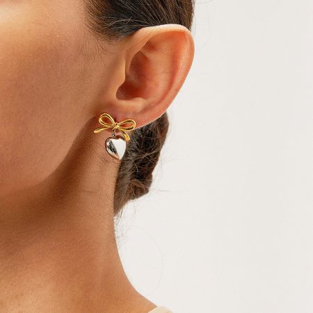 Detailed view of a single gold earring highlighting the bow and heart charm.