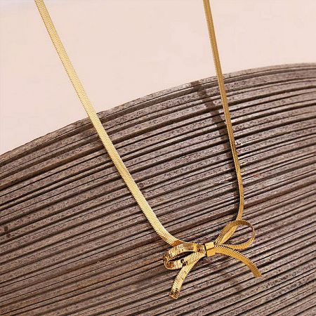 Close-up product shot of the gold bow necklace on a neutral background.
