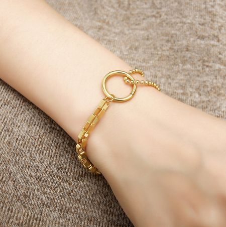 Close-up of the gold bracelet's circular clasp and mixed links.