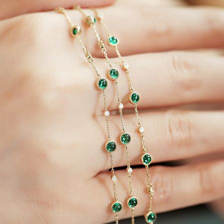 A delicate gold-plated sterling silver bracelet with emeralds on a hand.