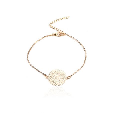 Detail view of the gold chain bracelet with a round floral-engraved disc charm.