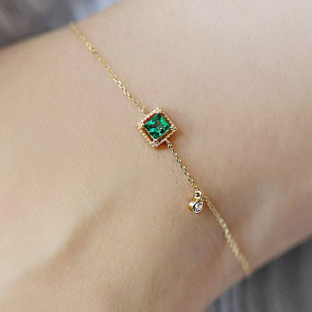 Close-up on wrist showing the delicate chain and sparkling green emerald zircon of the bracelet.