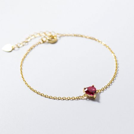 Elegant gold chain bracelet showcasing a brilliant heart-shaped red gemstone.