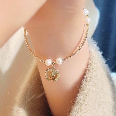 Detailed view of the 14K gold-plated bracelet showcasing the pearl and coin charm.