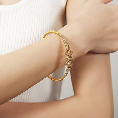 A stainless steel bangle with a unique spiral design and gold finish.