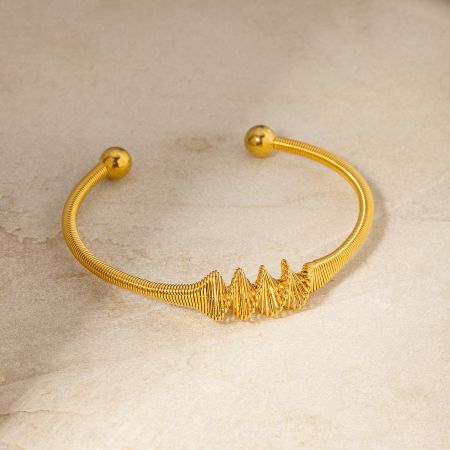 Close-up of a gold-finished stainless steel bangle with a distinctive wavy pattern.