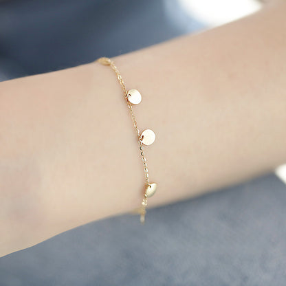 A gold bracelet from the set featuring white discs and heart-shaped spacers.