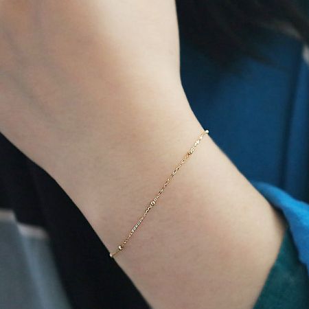 Close-up of the gold bead chain bracelet on a wrist, highlighting its delicate design and clasp.