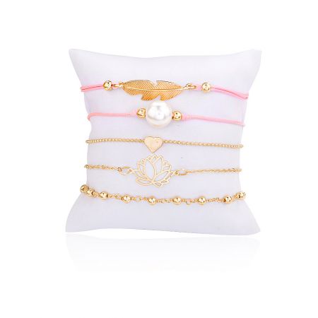 Set di braccialetti impilabili in oro riempito - Un set di cinque braccialetti impilabili in oro riempito con charm unici tra cui una piuma, una perla e un cuore, esposti su un cuscino bianco. Un braccialetto presenta una corda rosa.