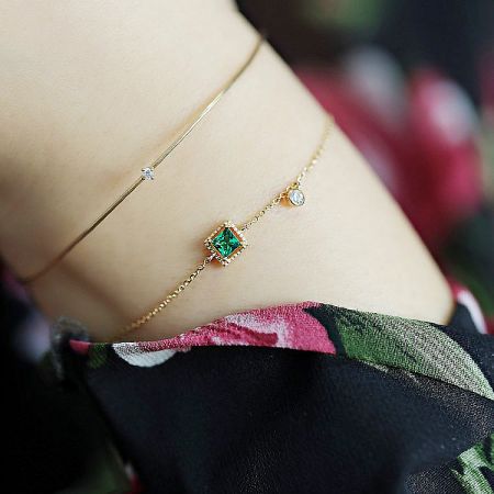 A set of two matching gold-plated bracelets with green and clear zircon stones.