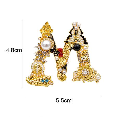 A pair of vintage initial brooches, letters 'A' and 'M', displayed to show their size and baroque style.