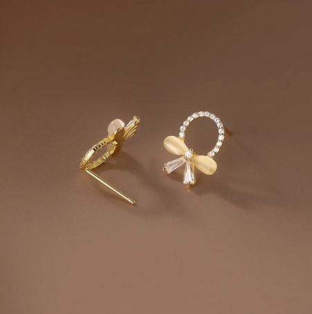 A pair of gold butterfly knot earrings with clear and white zirconia stones on a white background.