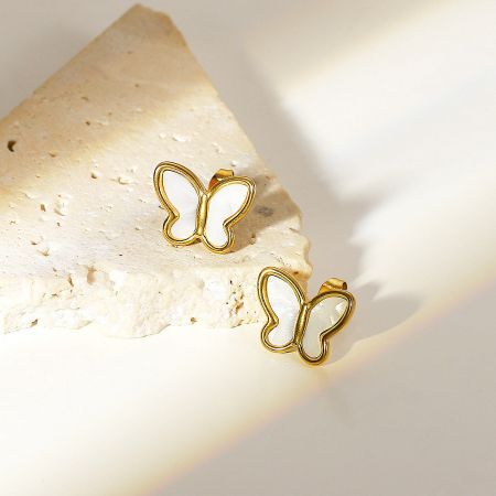 The gold butterfly stud earrings with mother of pearl inlay resting on a textured stone surface.