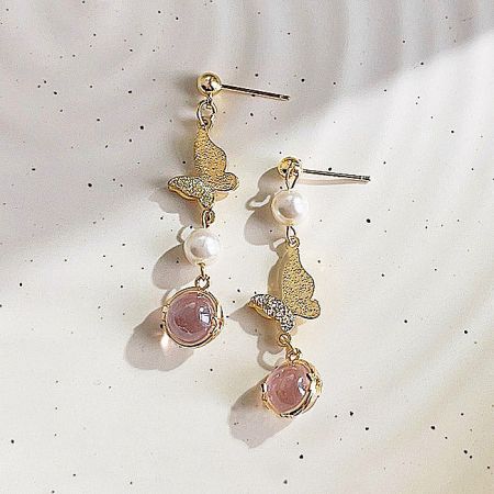 Detailed shot of the gold butterfly earrings showcasing the intricate pink gemstone and pearl details.