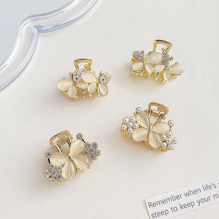 Collection of four gold-toned mini hair clips featuring butterfly and flower designs with pearls.