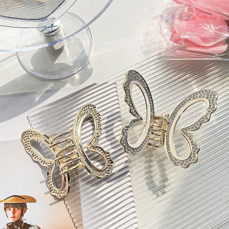 Two gold butterfly hair clips with intricate stone embellishments shown from a top-down angle.