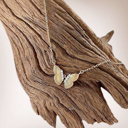 The gold butterfly necklace with textured wings displayed on a piece of driftwood.