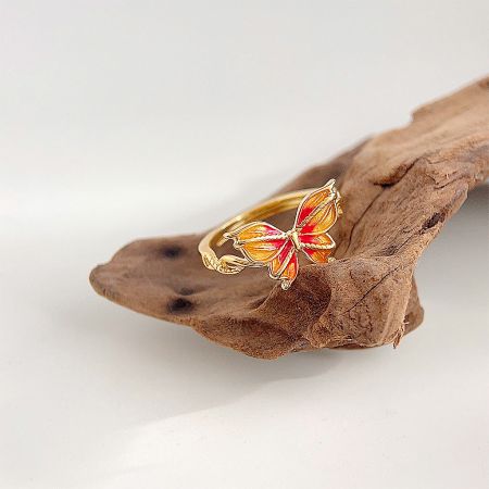 The orange and red enamel butterfly ring displayed on a piece of natural driftwood.