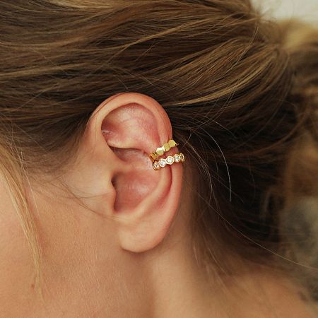 Detailed view of two gold cartilage ear cuffs from the mismatched set.